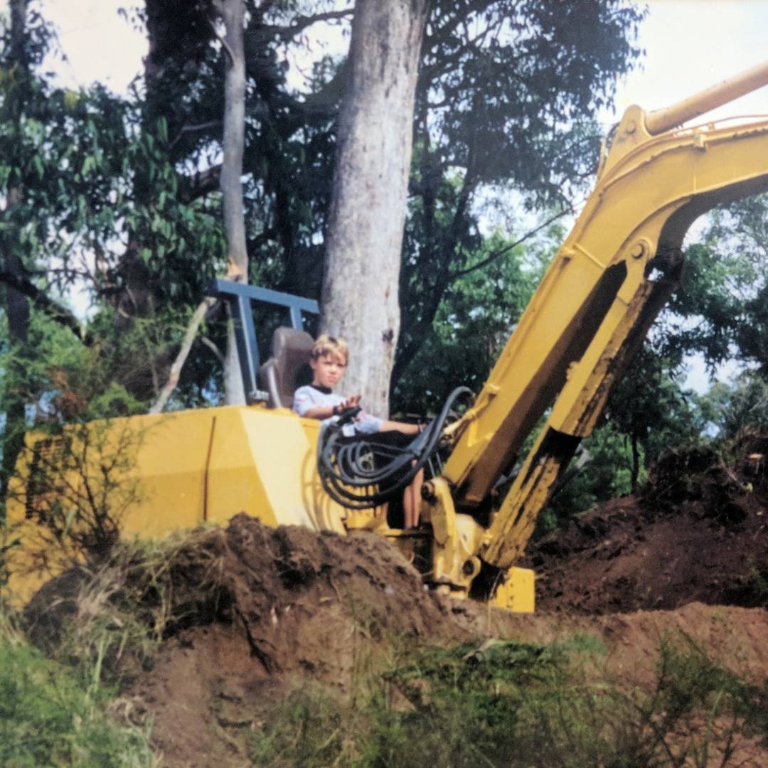 Childhood photograph of Daniel Goodman seated at the controls of a yellow excavator